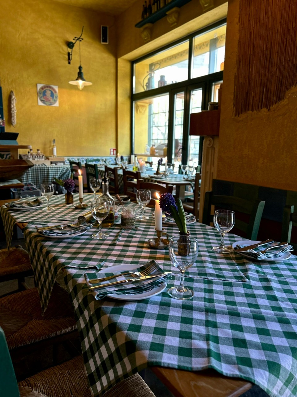 Gemütliches Restaurant mit karierten Tischdecken, Kerzen und gedeckten Tischen, warmes Licht.