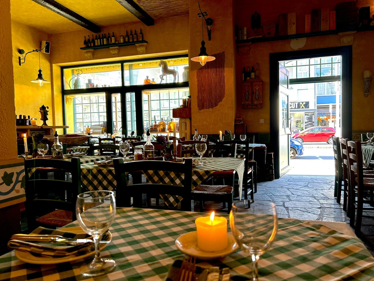 Gemütliches italienisches Restaurant mit karierten Tischdecken, Kerze und ein Fenster mit Straßenblick.