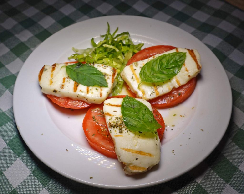 Gegrillter Käse auf Tomaten mit Basilikum auf Salat, auf einem karierten Tisch.