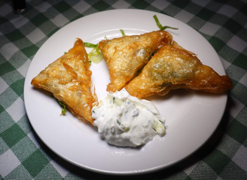 Drei knusprige Gebäckdreiecke mit grüner Füllung, serviert mit heller Sauce auf einem weißen Teller.