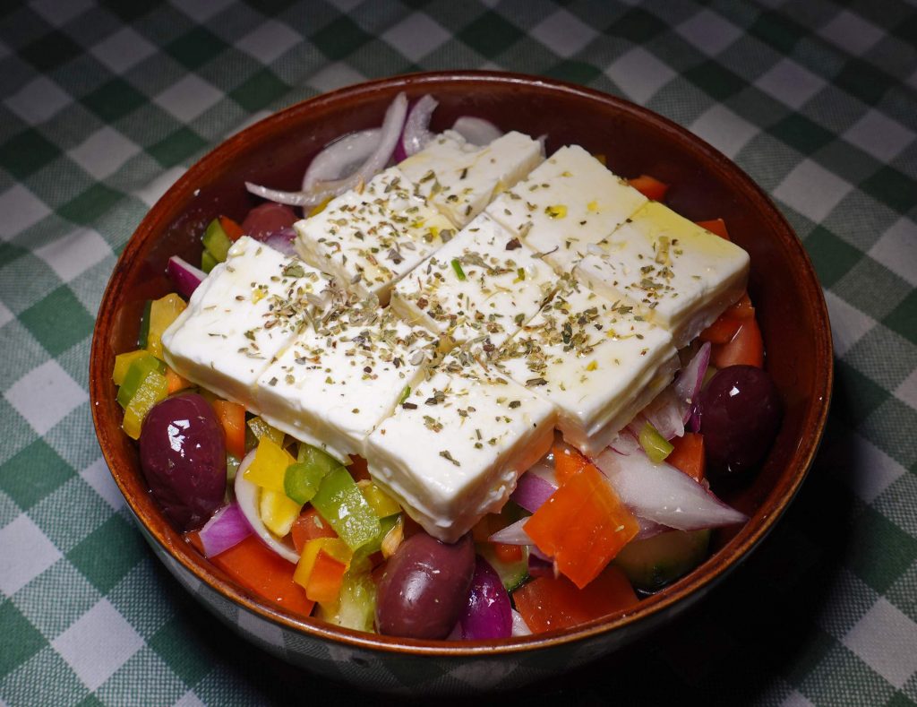 Ein griechischer Salat mit Feta, Oregano, Oliven, Gemüse in einer Schale auf kariertem Tuch.